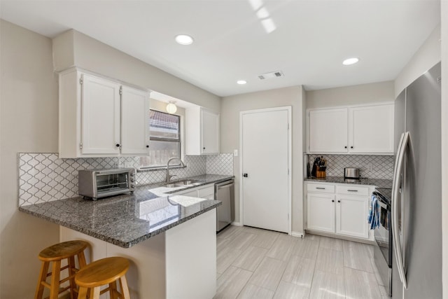 kitchen with stainless steel appliances, white cabinetry, dark stone counters, and kitchen peninsula