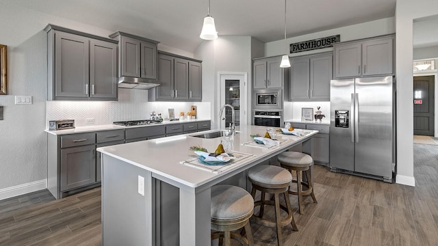 kitchen with a breakfast bar, sink, hanging light fixtures, appliances with stainless steel finishes, and a kitchen island with sink