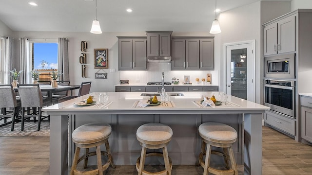 kitchen with stainless steel appliances, a breakfast bar area, a kitchen island with sink, and pendant lighting