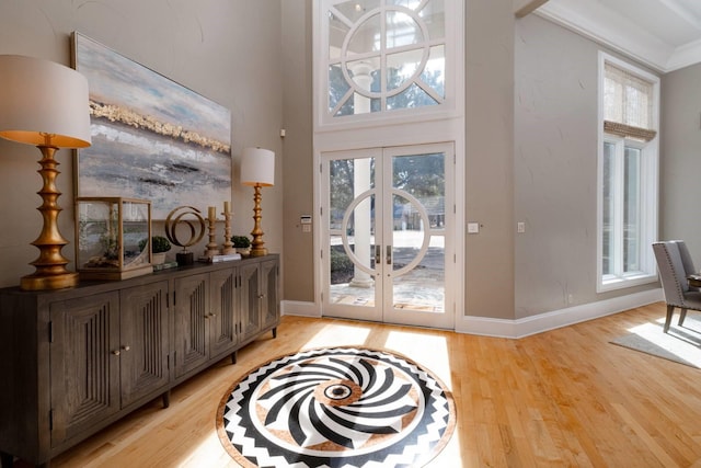 foyer with a towering ceiling, ornamental molding, light hardwood / wood-style floors, and french doors