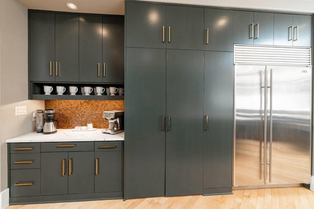 bar featuring stainless steel built in fridge, decorative backsplash, and light hardwood / wood-style flooring