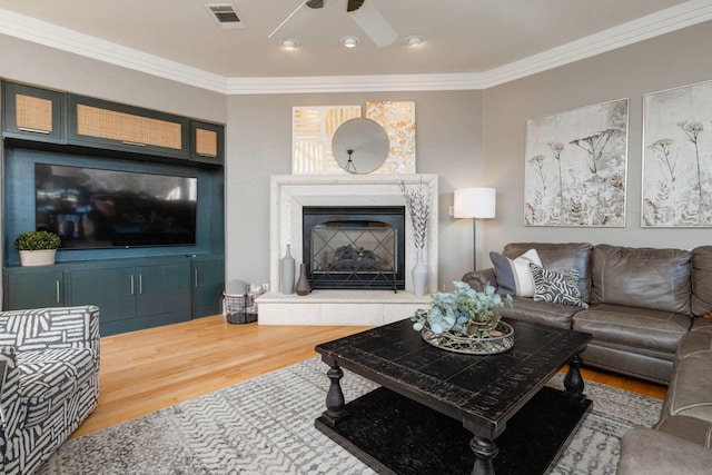 living room featuring a premium fireplace, crown molding, wood-type flooring, and ceiling fan