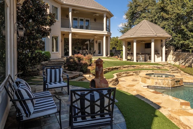 view of patio / terrace with a balcony, a swimming pool with hot tub, an outdoor hangout area, an outdoor bar, and ceiling fan