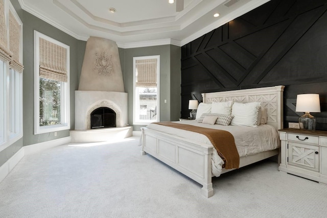 carpeted bedroom featuring a tray ceiling, a fireplace, ornamental molding, and ceiling fan