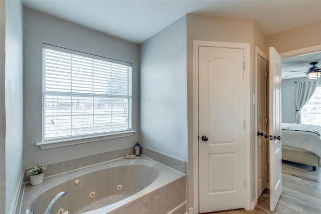 full bath with ensuite bathroom, a tub with jets, wood finished floors, and a wealth of natural light