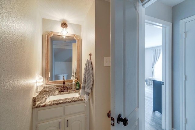 half bath with a textured wall, wood finished floors, and vanity