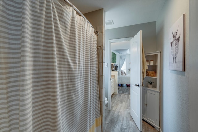 ensuite bathroom featuring curtained shower, ensuite bath, and wood finished floors