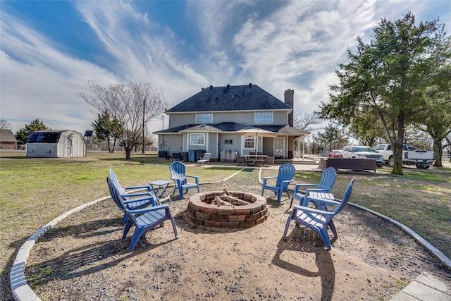 back of property featuring a storage shed, a fire pit, a chimney, a yard, and an outdoor structure