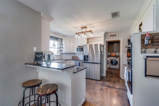 kitchen with dark countertops, visible vents, appliances with stainless steel finishes, washer and dryer, and a peninsula