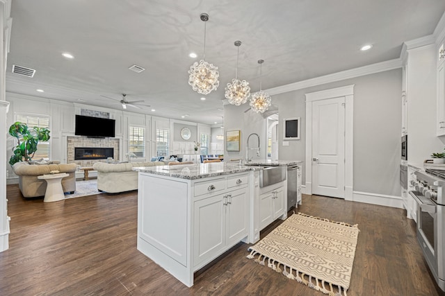 kitchen featuring stainless steel appliances, white cabinetry, light stone countertops, and a kitchen island with sink