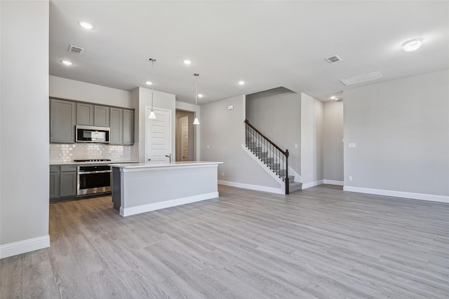 kitchen with gray cabinetry, hanging light fixtures, stainless steel appliances, a center island, and light wood-type flooring