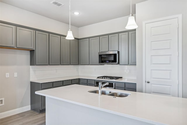 kitchen featuring appliances with stainless steel finishes, pendant lighting, tasteful backsplash, sink, and gray cabinetry