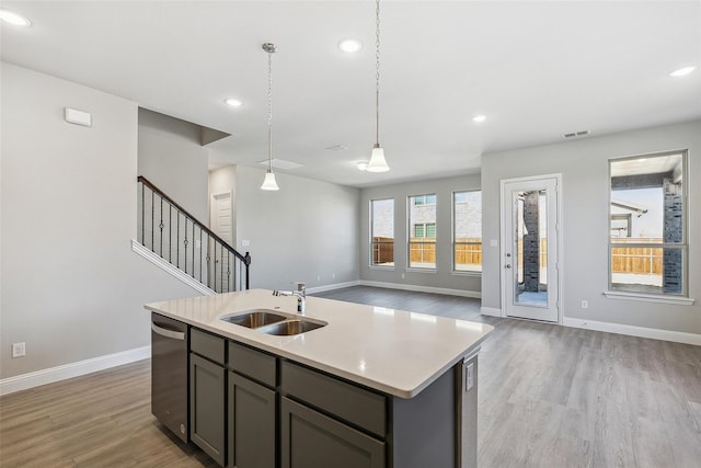 kitchen featuring pendant lighting, sink, stainless steel dishwasher, a center island with sink, and light wood-type flooring