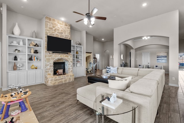 living room with dark wood-type flooring, ceiling fan, and a stone fireplace