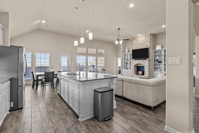 kitchen featuring pendant lighting, stainless steel appliances, light stone counters, an island with sink, and white cabinets