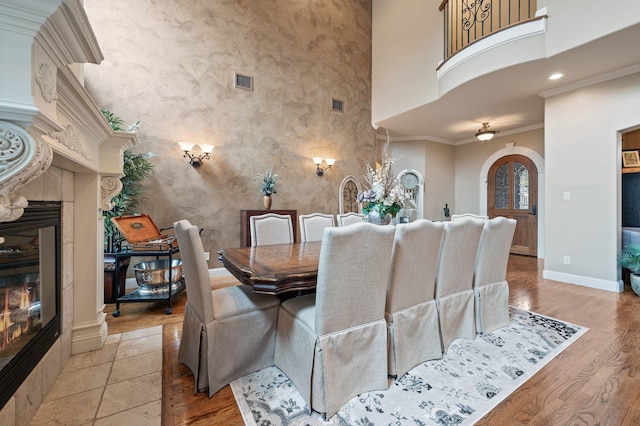 dining space with crown molding, a fireplace, a towering ceiling, and light wood-type flooring