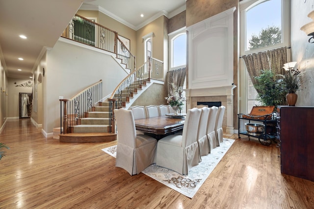 dining room with crown molding, a fireplace, light hardwood / wood-style floors, and a high ceiling