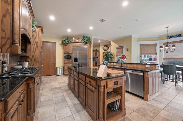 kitchen with pendant lighting, sink, built in appliances, a center island with sink, and dark stone counters