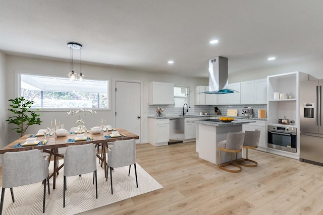 kitchen with a kitchen island, appliances with stainless steel finishes, island range hood, decorative light fixtures, and white cabinetry