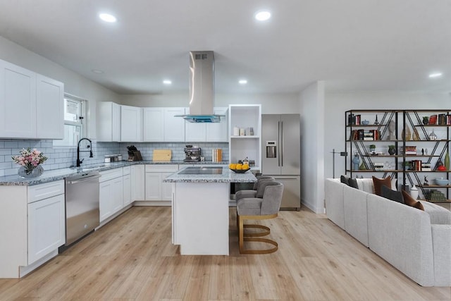 kitchen featuring a kitchen island, white cabinetry, island exhaust hood, light stone counters, and stainless steel appliances