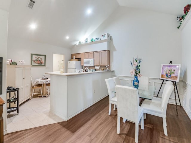 dining space featuring high vaulted ceiling and light hardwood / wood-style flooring