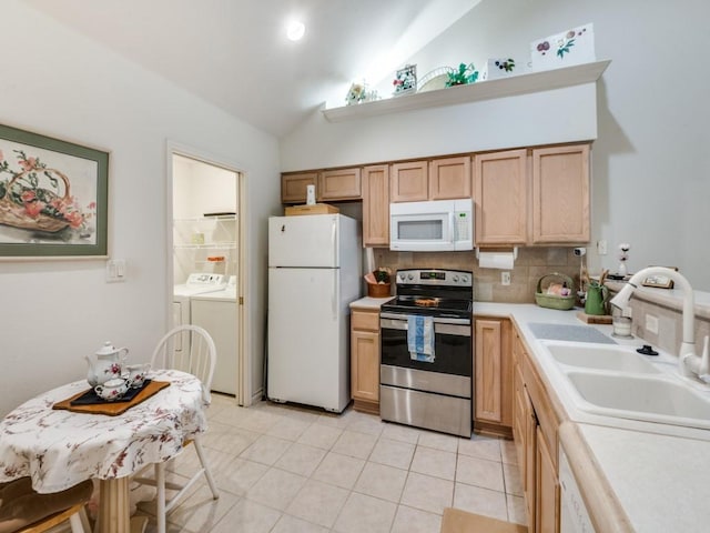 kitchen featuring lofted ceiling, sink, light tile patterned floors, white appliances, and washing machine and dryer