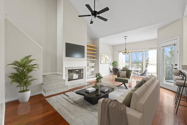 living room featuring hardwood / wood-style floors, ceiling fan with notable chandelier, a tile fireplace, and high vaulted ceiling