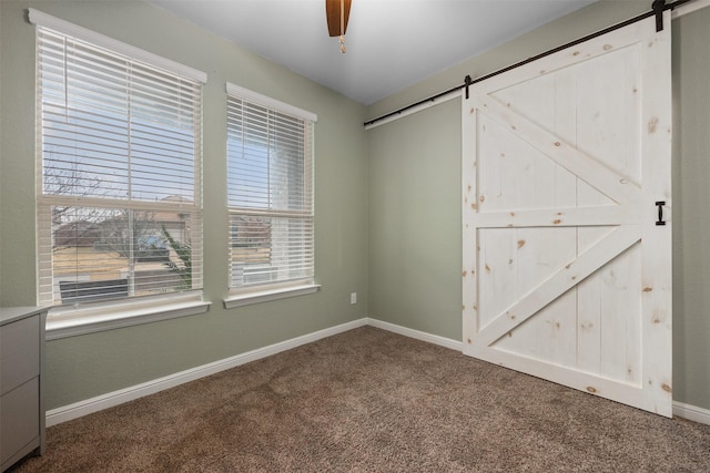 unfurnished bedroom featuring ceiling fan, a barn door, and carpet floors