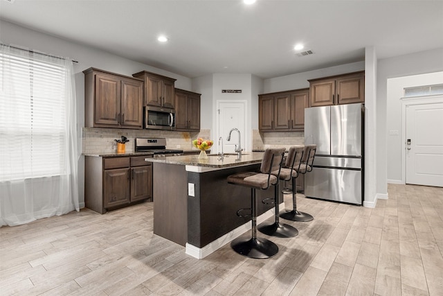 kitchen featuring a breakfast bar, sink, light stone counters, appliances with stainless steel finishes, and a kitchen island with sink