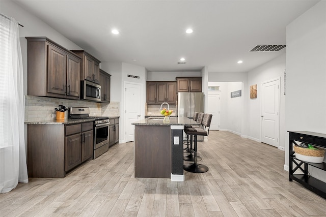 kitchen featuring sink, a breakfast bar, appliances with stainless steel finishes, a kitchen island with sink, and light stone counters