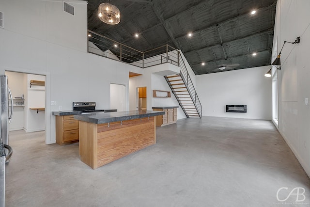 kitchen with a towering ceiling, a kitchen island, stainless steel appliances, a kitchen bar, and light brown cabinetry