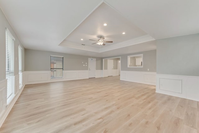 unfurnished living room featuring ceiling fan, ornamental molding, light wood-type flooring, and a tray ceiling