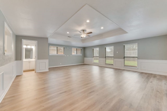 unfurnished living room with a tray ceiling, light hardwood / wood-style flooring, and ceiling fan