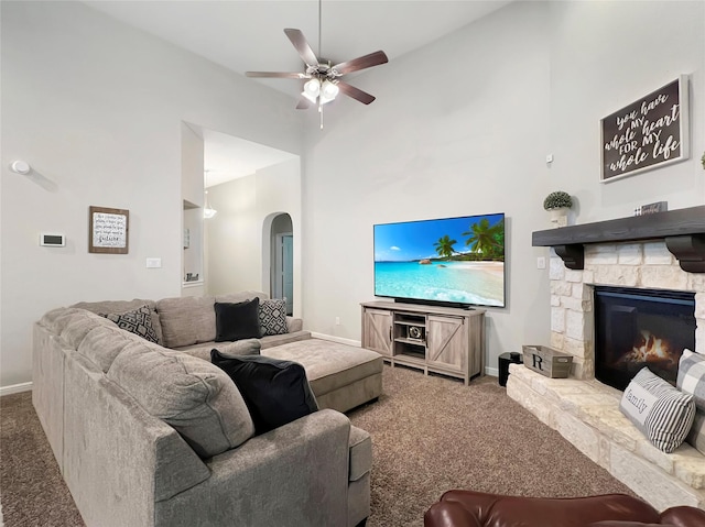 living room with ceiling fan, carpet, a stone fireplace, and high vaulted ceiling