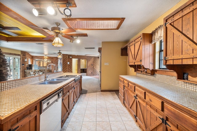 kitchen with sink, tile countertops, light tile patterned floors, dishwasher, and ceiling fan