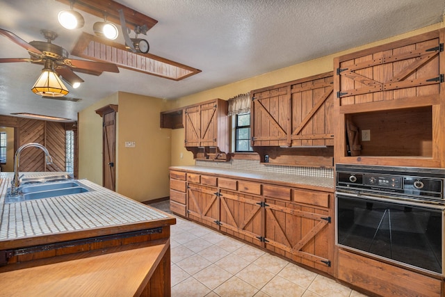 kitchen with sink, a textured ceiling, light tile patterned floors, ceiling fan, and wall oven