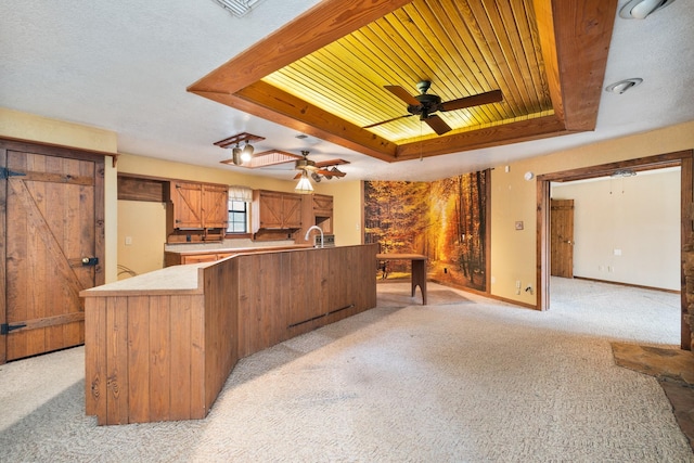 kitchen with wood ceiling, ceiling fan, a tray ceiling, light colored carpet, and kitchen peninsula