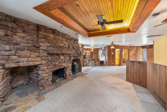 unfurnished living room featuring a stone fireplace, wood ceiling, ceiling fan, a raised ceiling, and light colored carpet