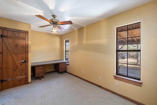 unfurnished bedroom featuring a textured ceiling, built in desk, light colored carpet, and ceiling fan