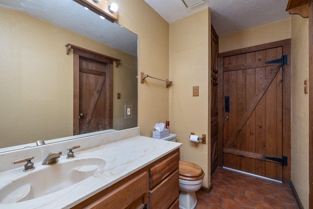 bathroom featuring vanity, toilet, tile patterned flooring, and a textured ceiling