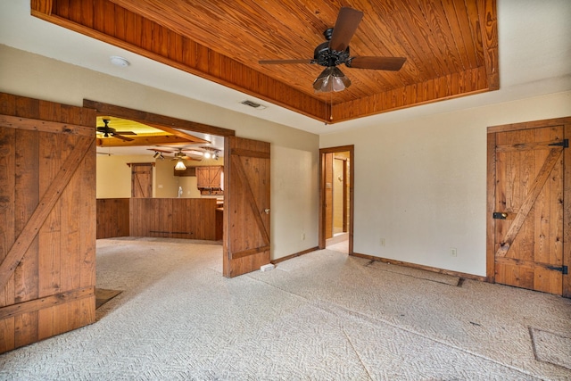 carpeted spare room featuring ceiling fan, a raised ceiling, wooden ceiling, a barn door, and wood walls