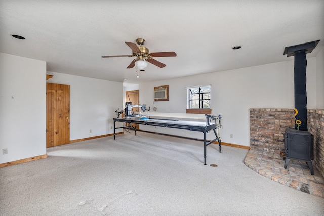 recreation room featuring a wall unit AC, carpet, ceiling fan, and a wood stove