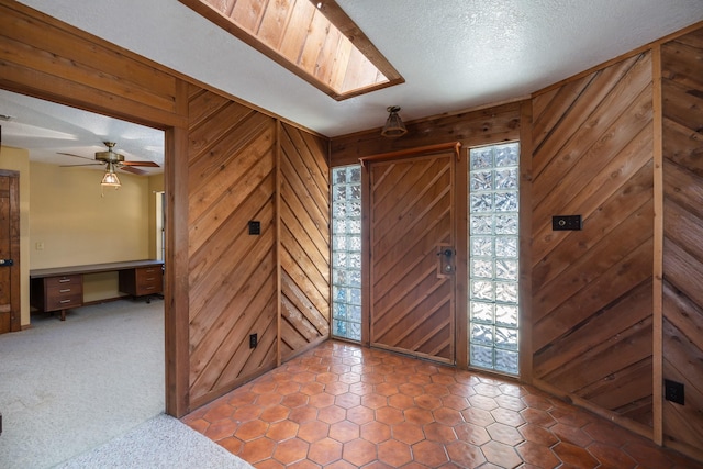 carpeted foyer featuring ceiling fan, built in desk, wooden walls, and a textured ceiling