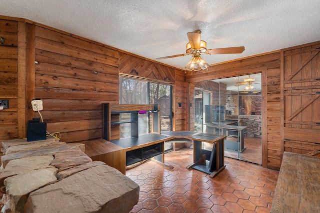 living room with ceiling fan, a textured ceiling, and wood walls