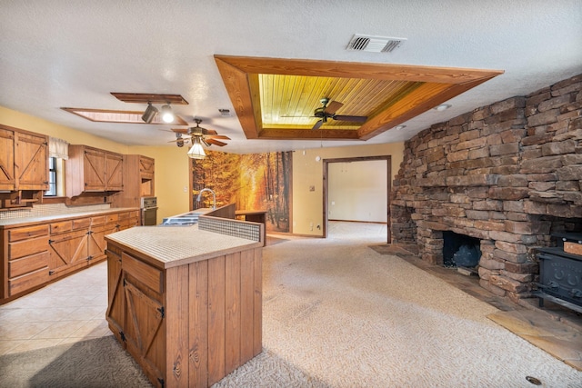 kitchen featuring a tray ceiling, a textured ceiling, a kitchen island, light carpet, and a wood stove