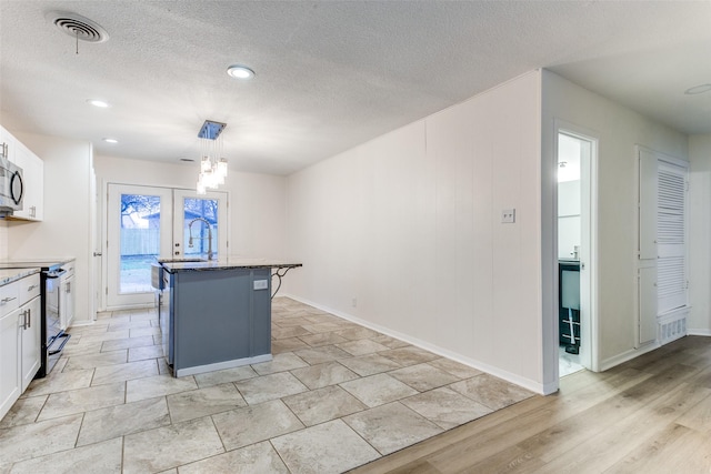 kitchen with white cabinetry, decorative light fixtures, a kitchen island with sink, and range with electric stovetop