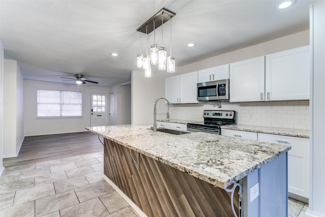 kitchen featuring decorative light fixtures, sink, white cabinets, stainless steel appliances, and a center island with sink