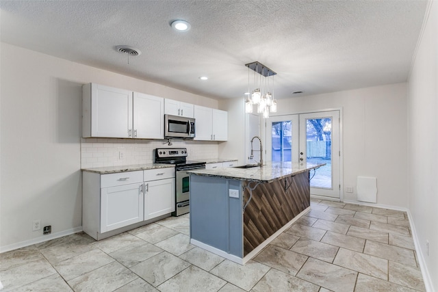 kitchen with light stone counters, decorative light fixtures, a center island with sink, stainless steel appliances, and white cabinets