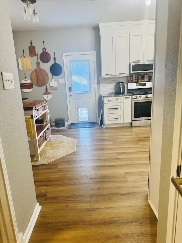 kitchen with appliances with stainless steel finishes, white cabinets, and light hardwood / wood-style flooring