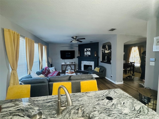 living room with a healthy amount of sunlight, dark wood-type flooring, ceiling fan, and a textured ceiling